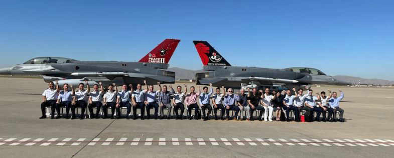 a group of people posing for a photo seated in chairs in front of a plane